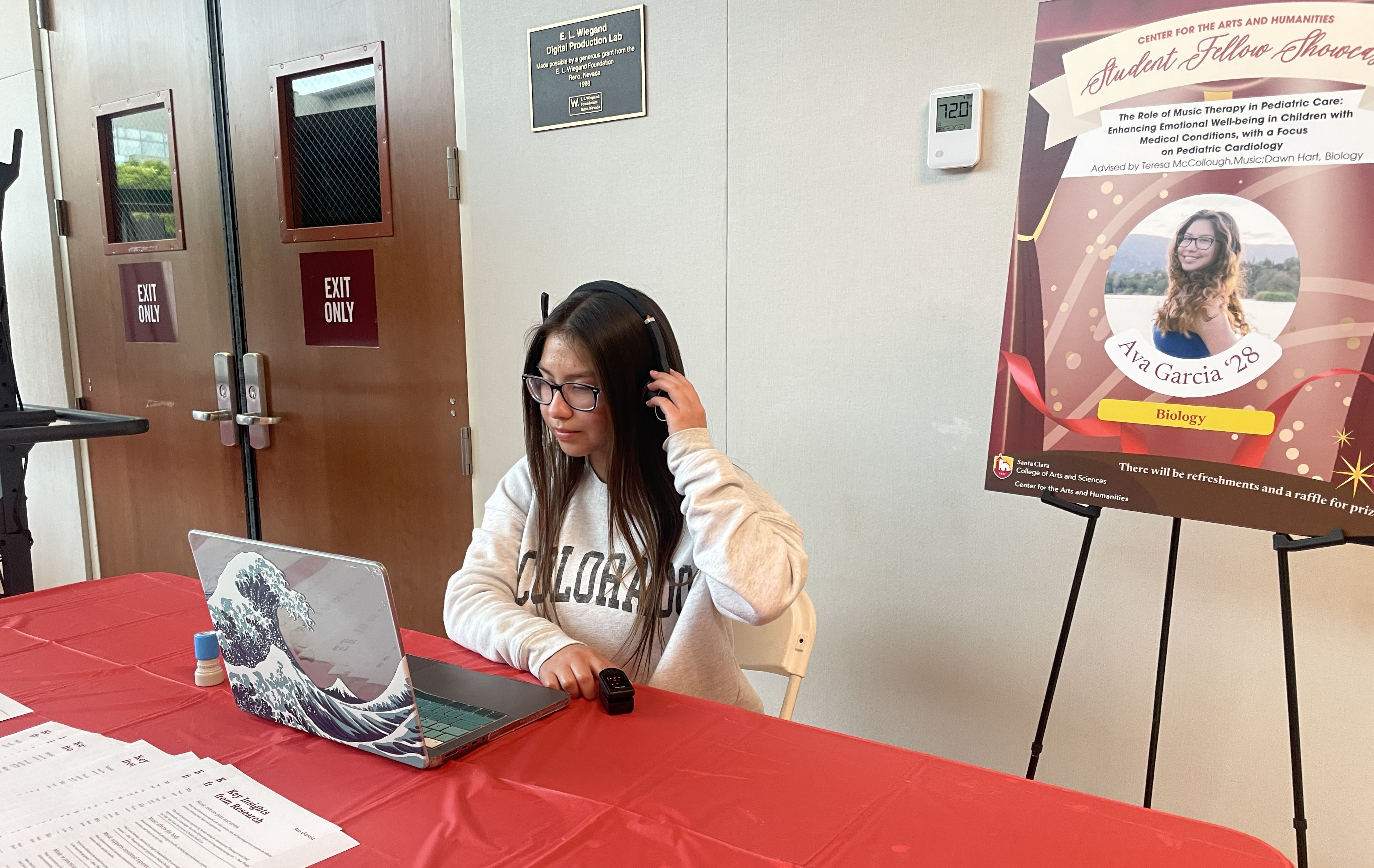 Student listens to music through headphones while using a laptop and pulse oximeter.