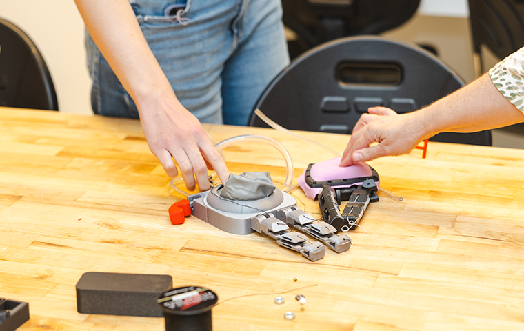 Two hands press robotic prosthetic sensors on a lab table.