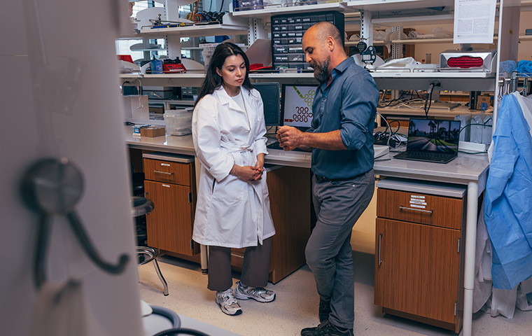 Rana Altay and Emre Araci chat standing in a lab space