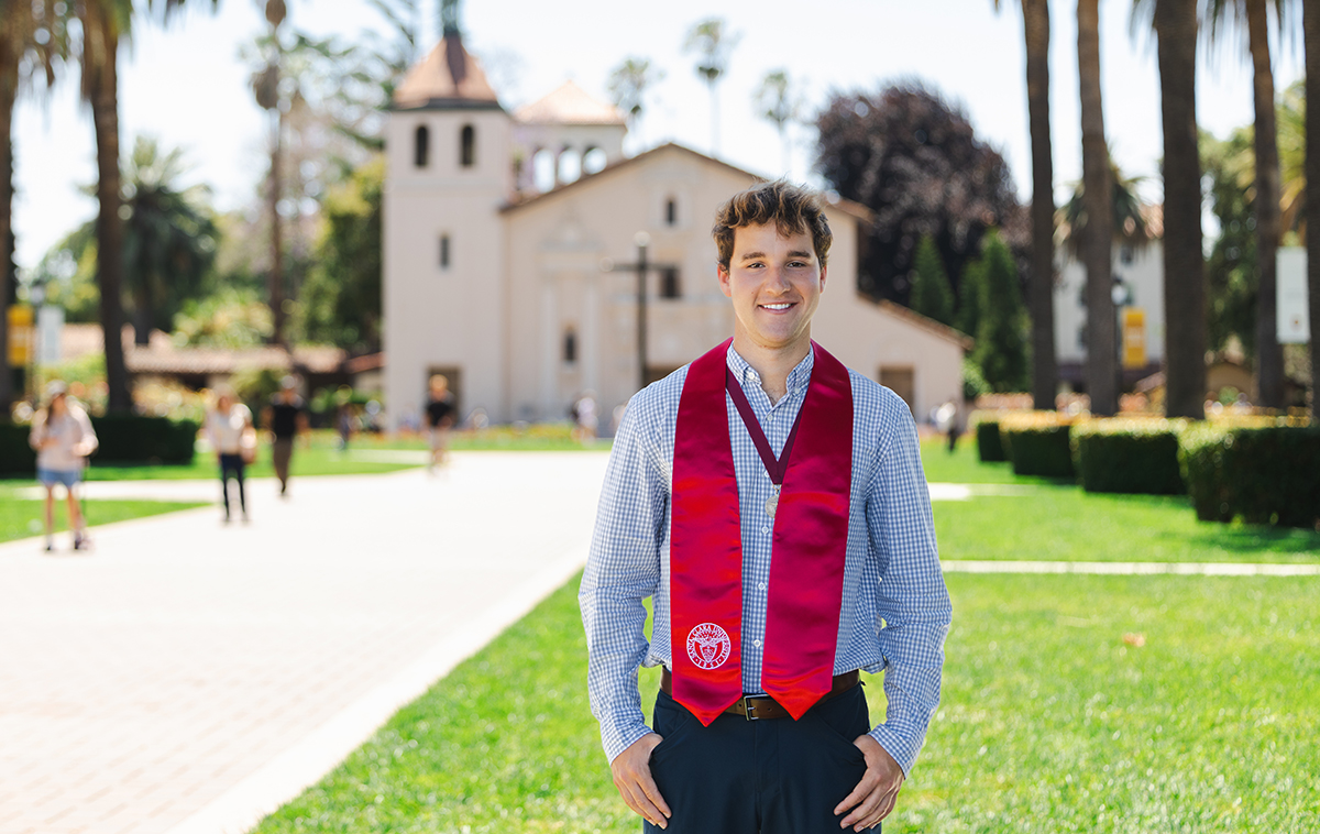 Valedictorian Charles Silver in a button up shirt with commencement scarf on Palm Drive with Mission Church in background