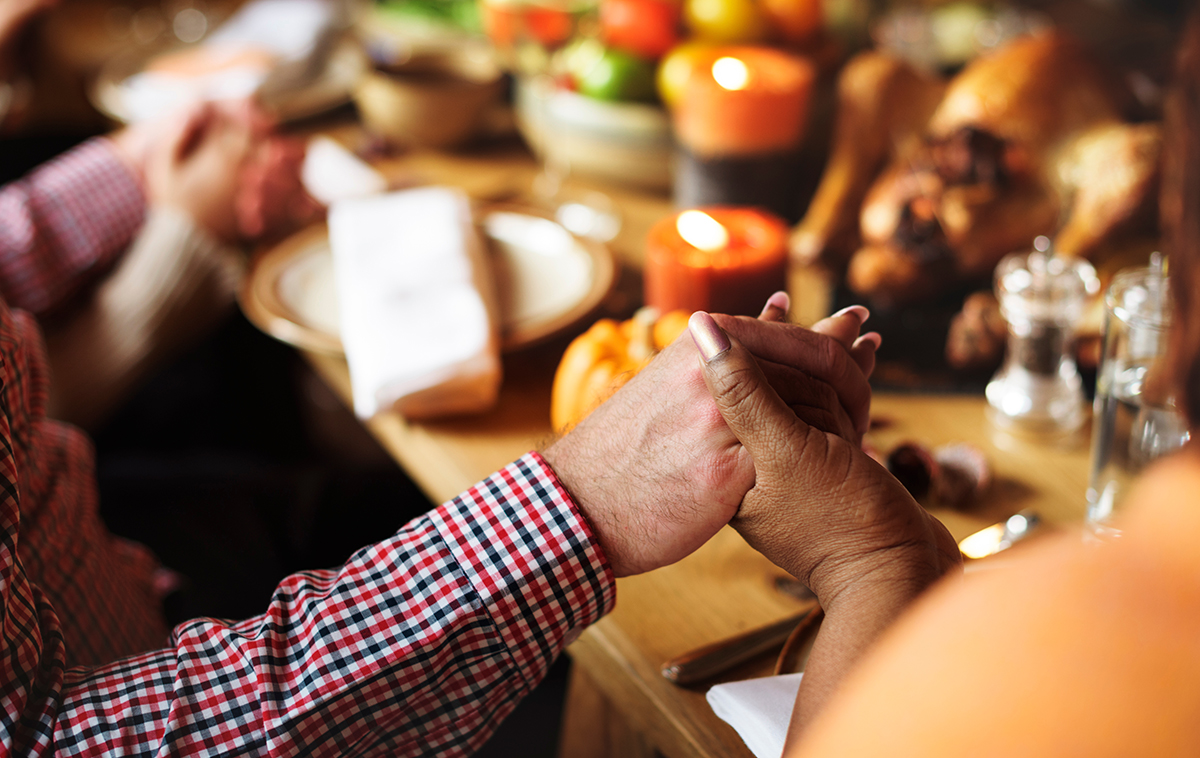 A man and womans hand come together in prayer at Thanksgiving dinner table.