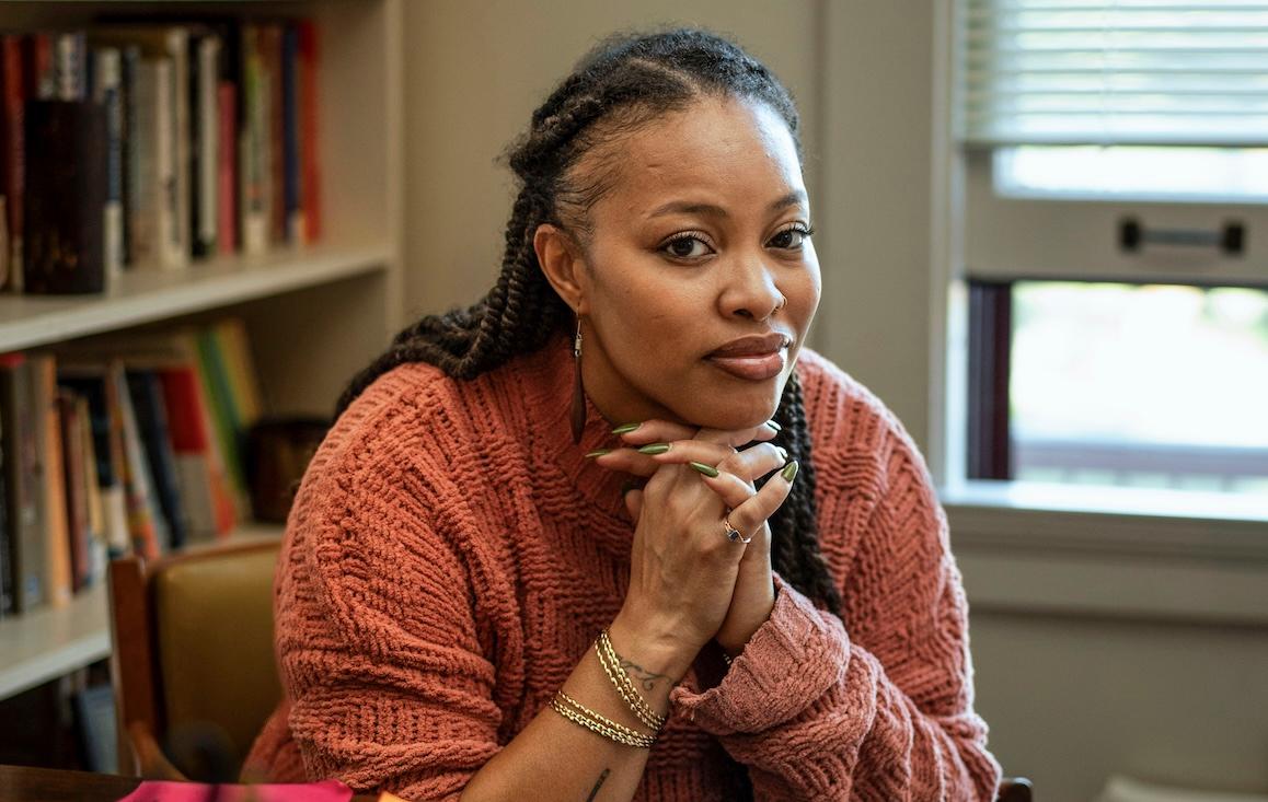 Professor Kai Harris sits at her desk in an orange sweater.