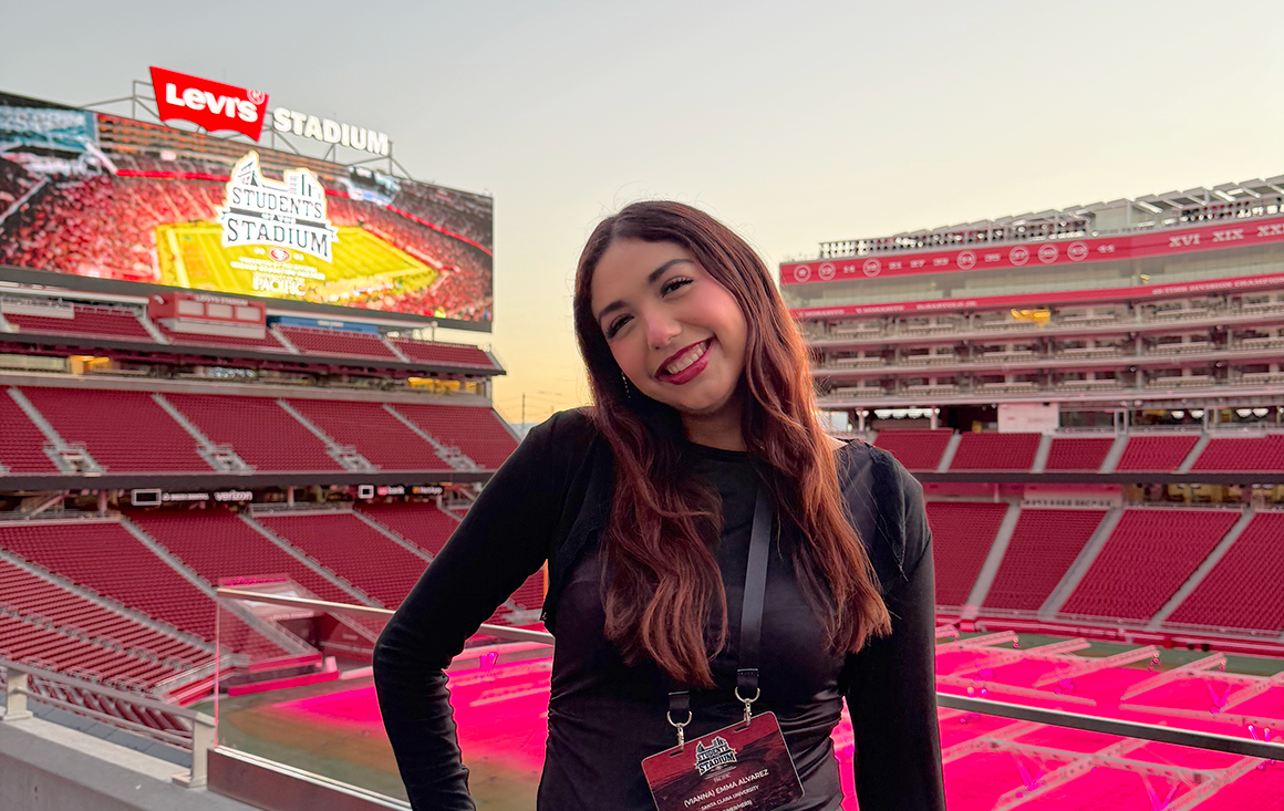 A young Latina woman poses in the 49ers-red Levis Stadium at dusk.