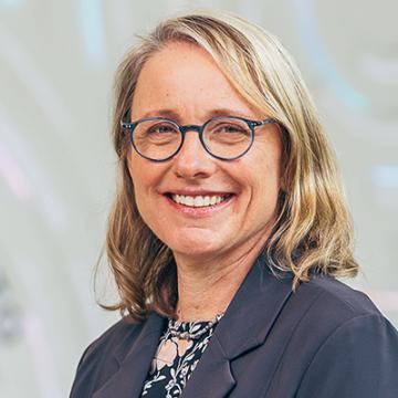 Engineering Dean Kendra Sharp headshot in gray blazer in front of donor wall in SCDI