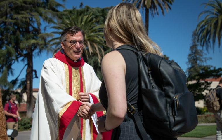 Fr. OBrien in clerical garb shaking hand of female student, seen from behind student