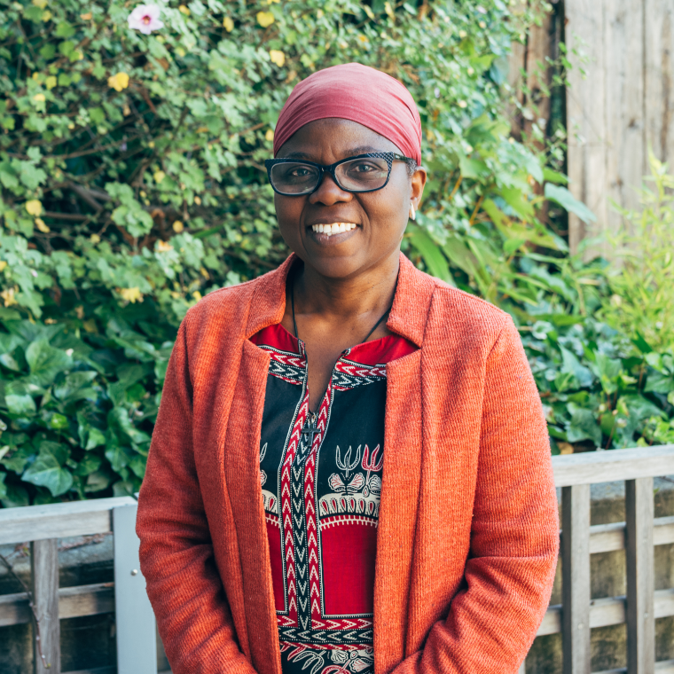Women with glasses looking at the camera with a green and natural background behind her.