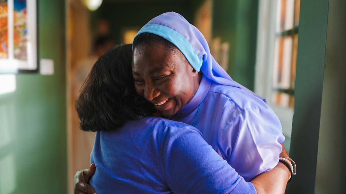 Two women embracing. One is wearing a blue habit.