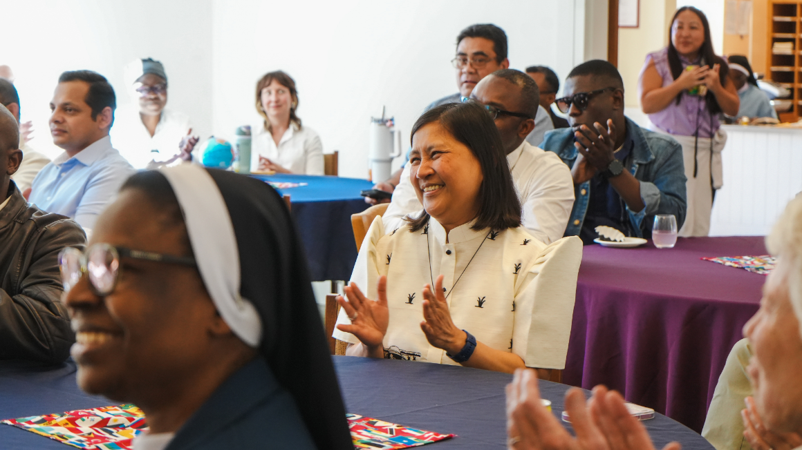 A group of people smiling and clapping. The photo focuses on a woman in the center.