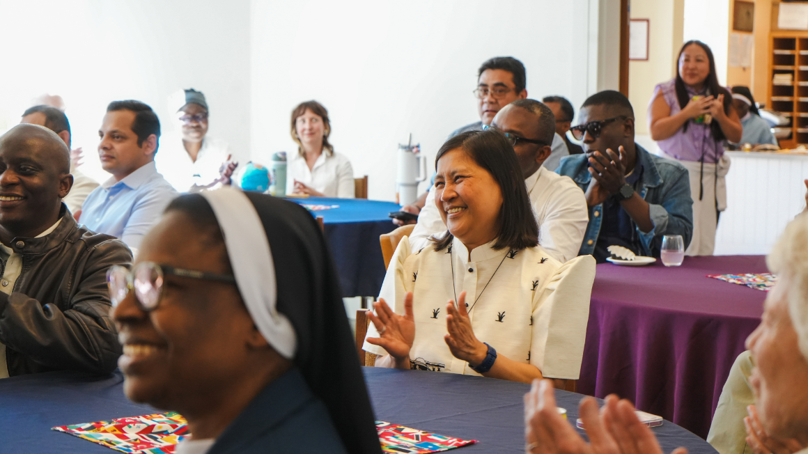 A group of people smiling at round tables. The focus is on a woman smiling and clapping.