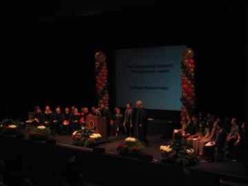 Large group on stage with lighting and a central screen displaying 2012 OSE.
