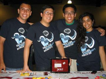 Four team members wearing matching SCEO shirts pose together behind a table.