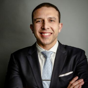 A person wearing a suit, smiling with arms crossed.