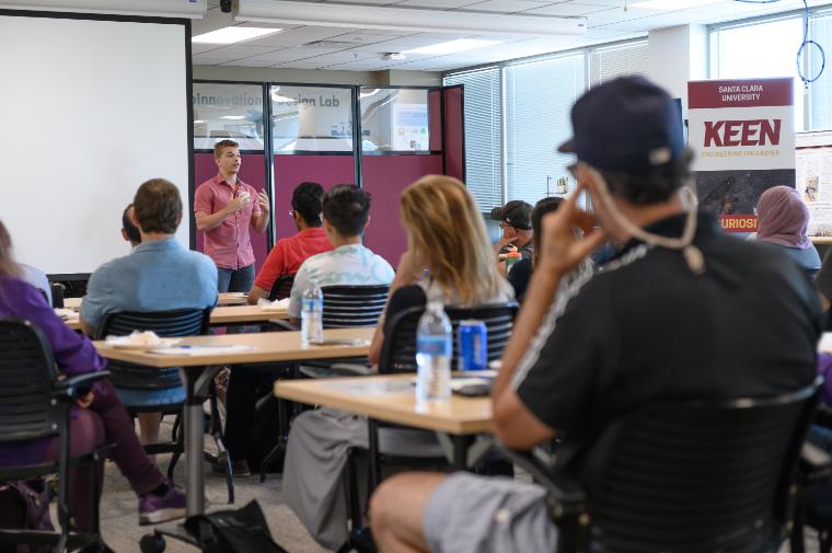 Classroom setting with an instructor speaking to students at desks.
