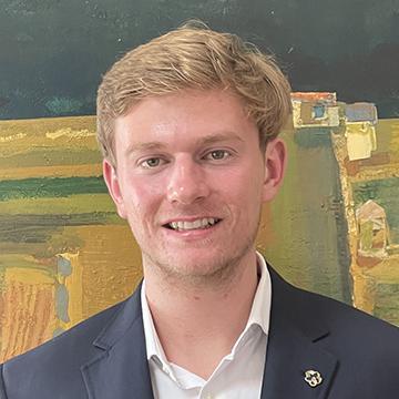 Man in dark suit jacket and white shirt smiling