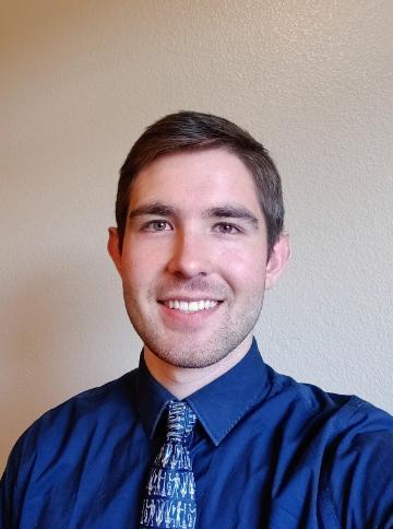 A man in a blue shirt and patterned tie, smiling.