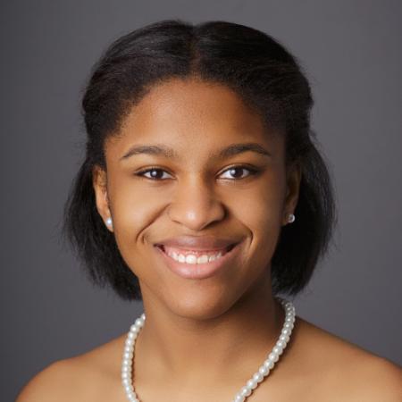 A person smiling in formal attire with a pearl necklace.