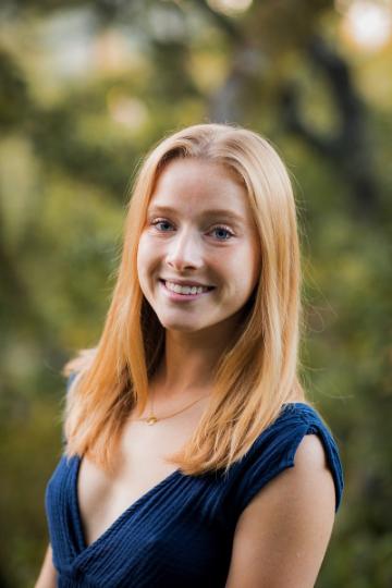 A person wearing a dark blue top, smiling in an outdoor setting.