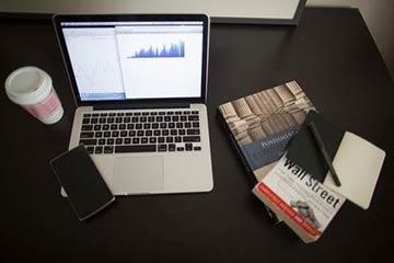 Laptop, coffee cup, open books, and papers on a dark desk.