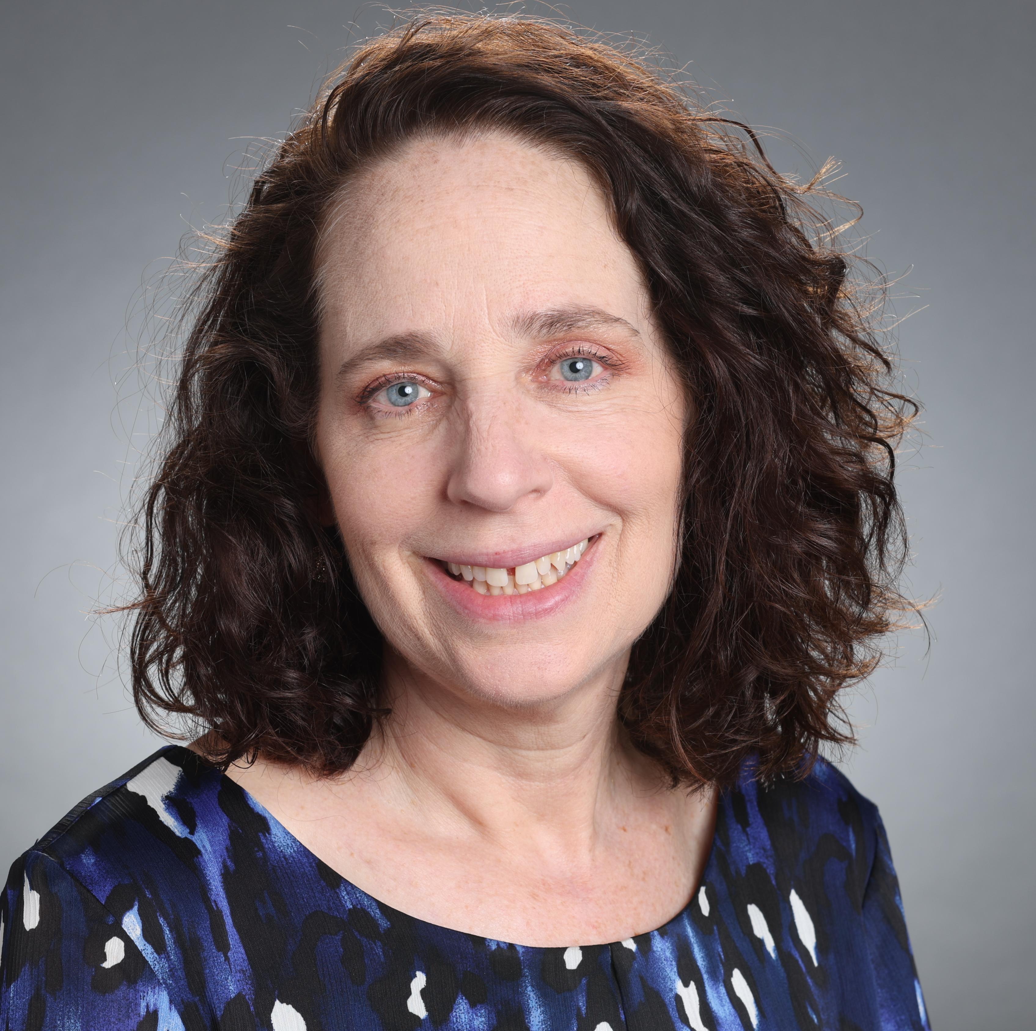 A person smiling against a gray background.