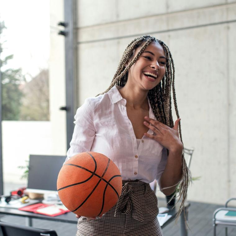A cheerful young businesswoman having fun with ball in office