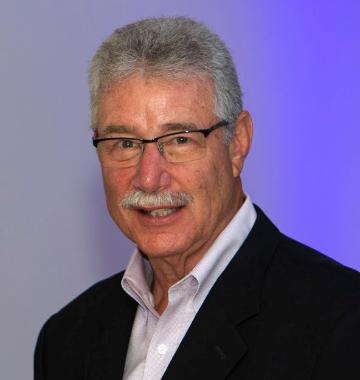 A man in a suit and glasses against a purple background.