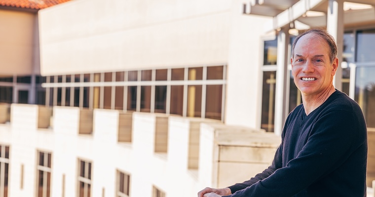Kris Mitchener standing on the balcony of Lucas Hall with the building curving around to the left in the background. image link to article