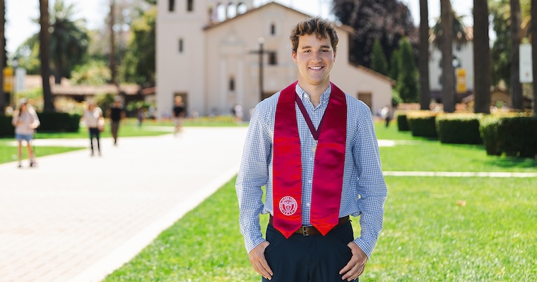 Valedictorian Charles Silver in a button up shirt with commencement scarf on Palm Drive with Mission Church in background