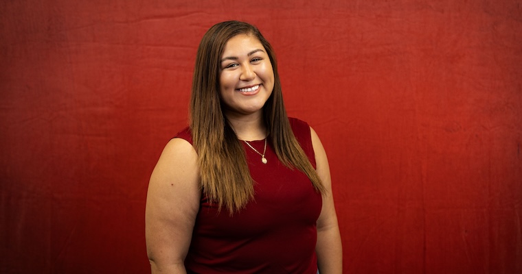 Young woman smiles in front of red backdrop. image link to article