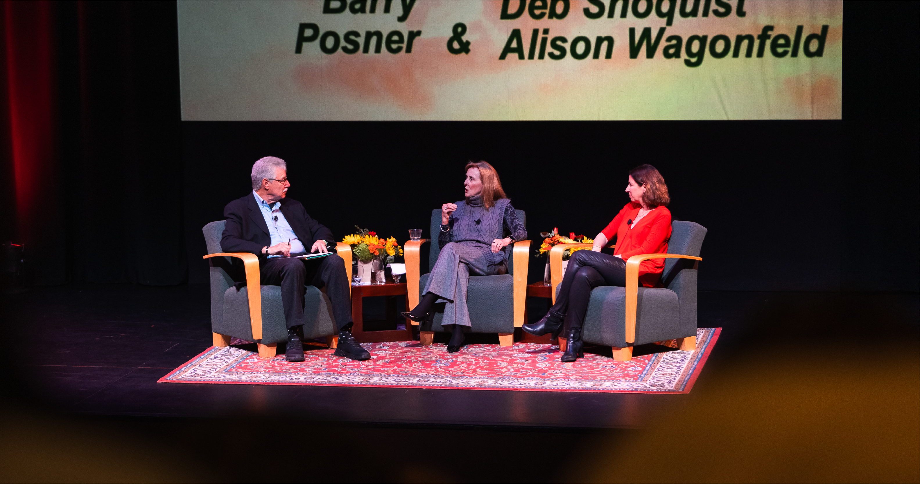 Three people are seated on stage in armchairs engaged in a discussion as part of Leavey Power of Purpose series