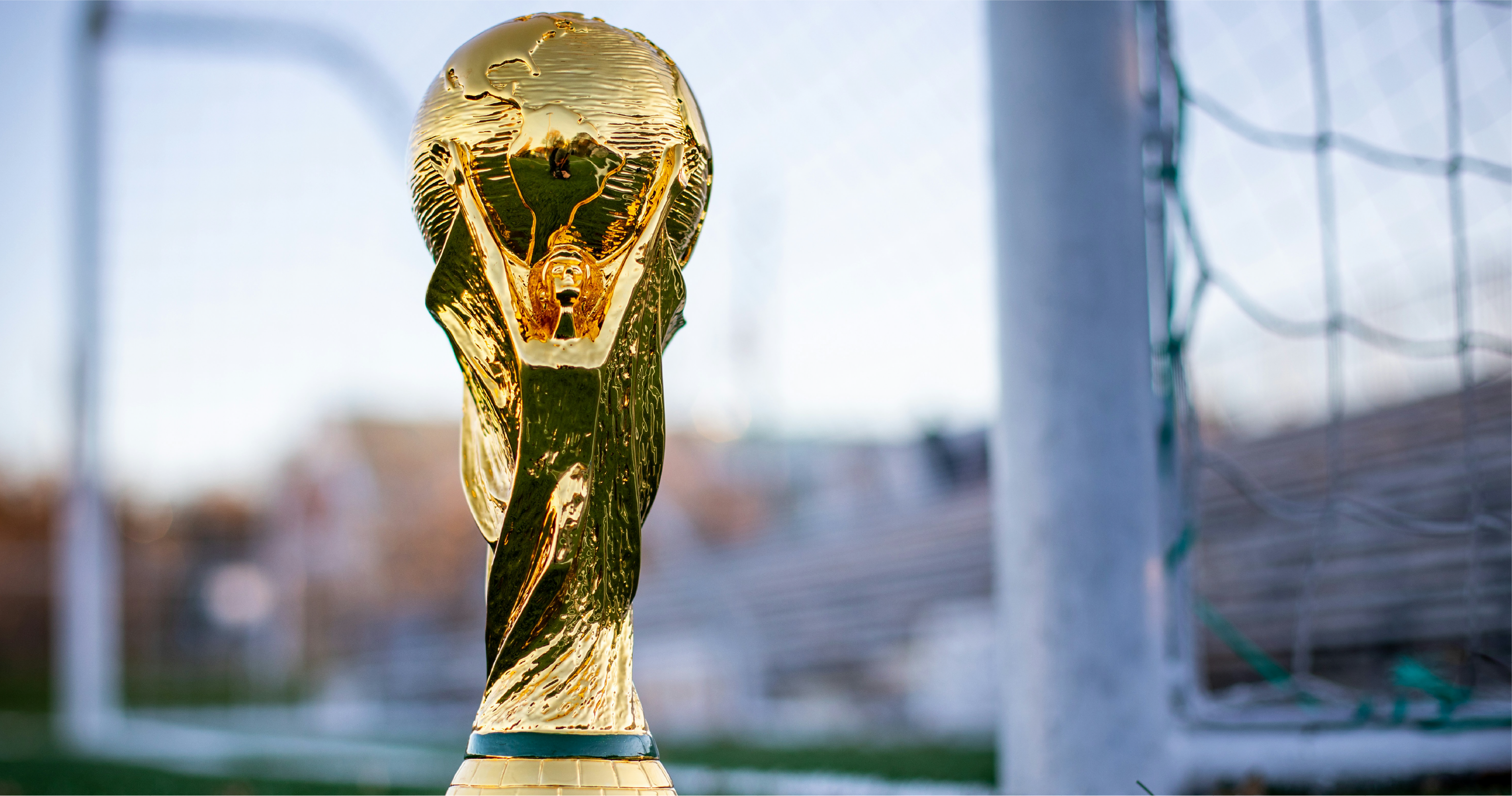 World cup trophy with soccer goal in the background.