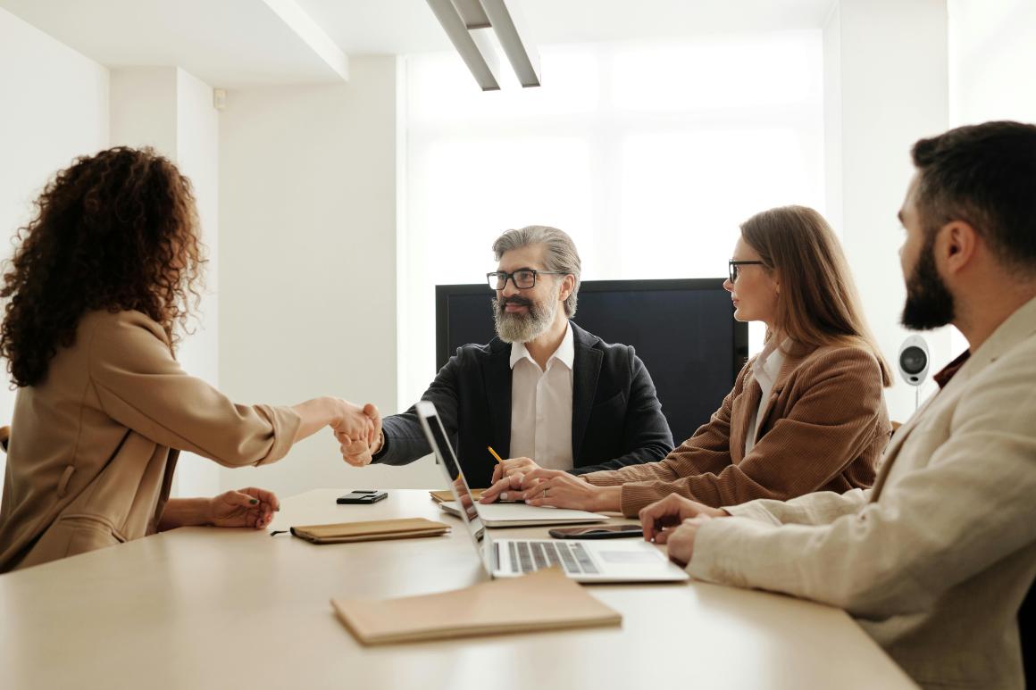 Handshake deal at business conference table with two colleagues looking on