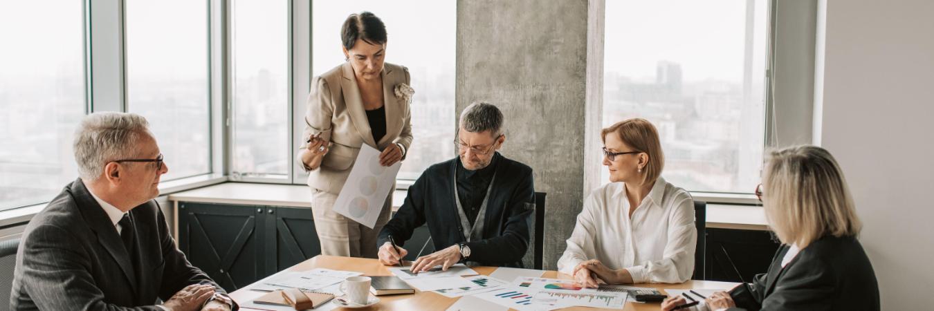 Business professionals meet around a conference table while reviewing charts and documents in a modern office.