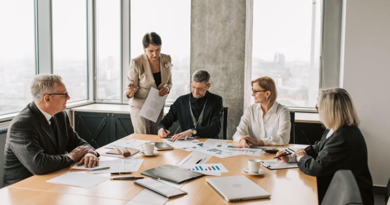 Business professionals meet around a conference table while reviewing charts and documents in a modern office.