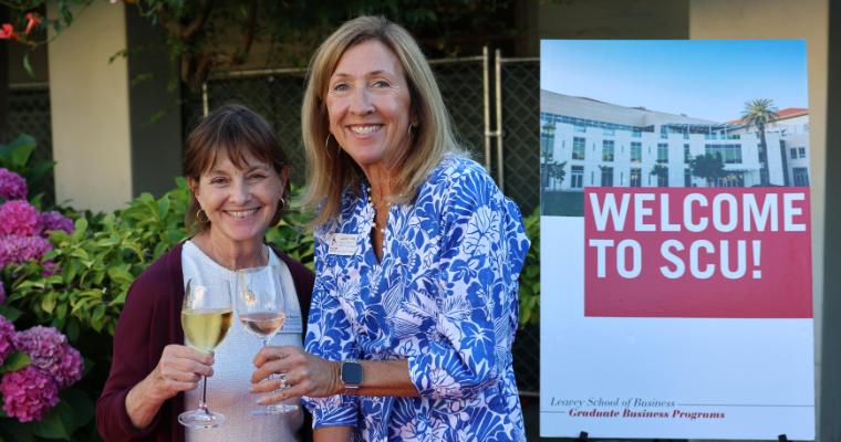Two admissions advisors toast with wine glasses outdoors at graduate business new student welcome. image link to article