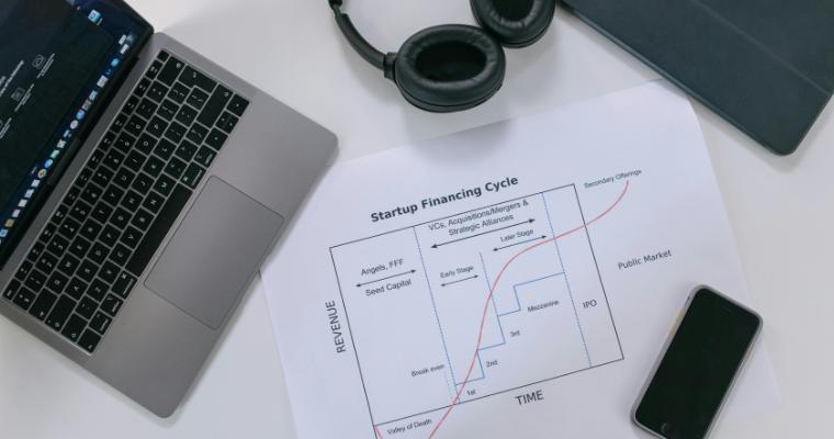 Flat lay of a modern workspace with tech gadgets and a startup financing cycle chart