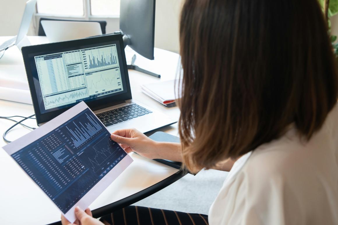 Looking at graphs on paper and laptop over shoulder