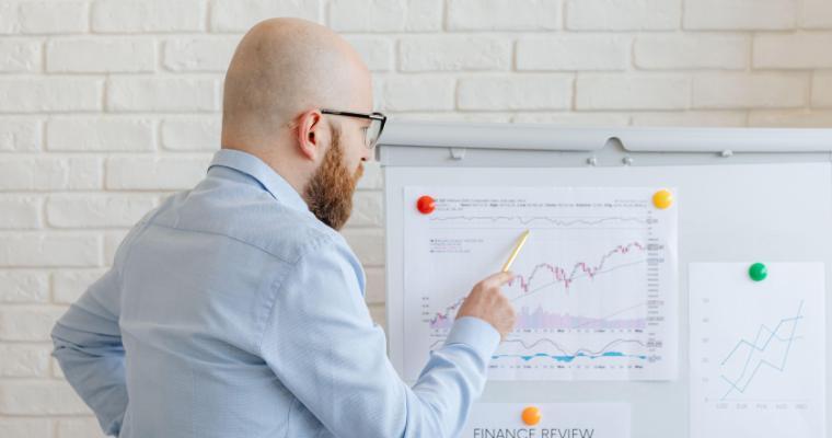 Man pointing to financial charts on a presentation board, including a page titled FINANCE REVIEW.