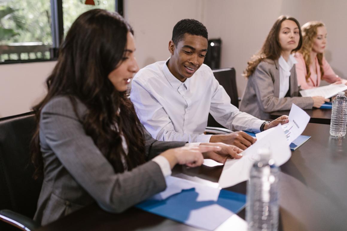 A diverse group of four professionals in a conference room, discussing documents at a table with water bottles.