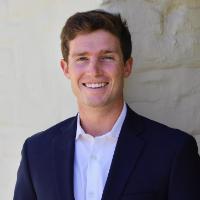 A person smiling in formal attire outdoors.