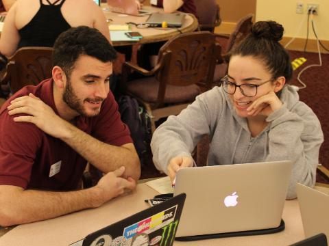 Two people sitting at a table working on a laptop.