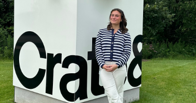 Retail Studies minor student standing beside a large white Crate & Barrel sign on a grassy lawn.