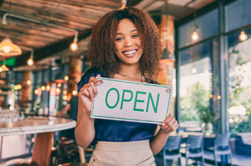 Young woman holding an open sign in her business