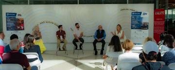 Five panelists are engaged in discussion, sitting in front of an audience