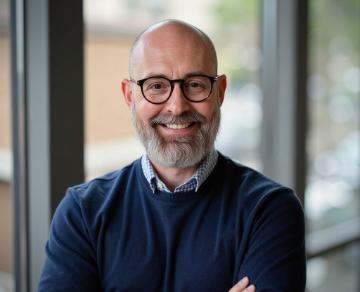 Man named Juan Reyes with glasses, bald head and sweater