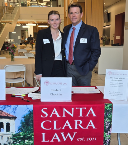 A man and a young woman in business wear standing behind an event check-in table with a banner reading Santa Clara Law. The mans nametag reads Hon. Stuart Scott and the young womans reads Morgan Scott.