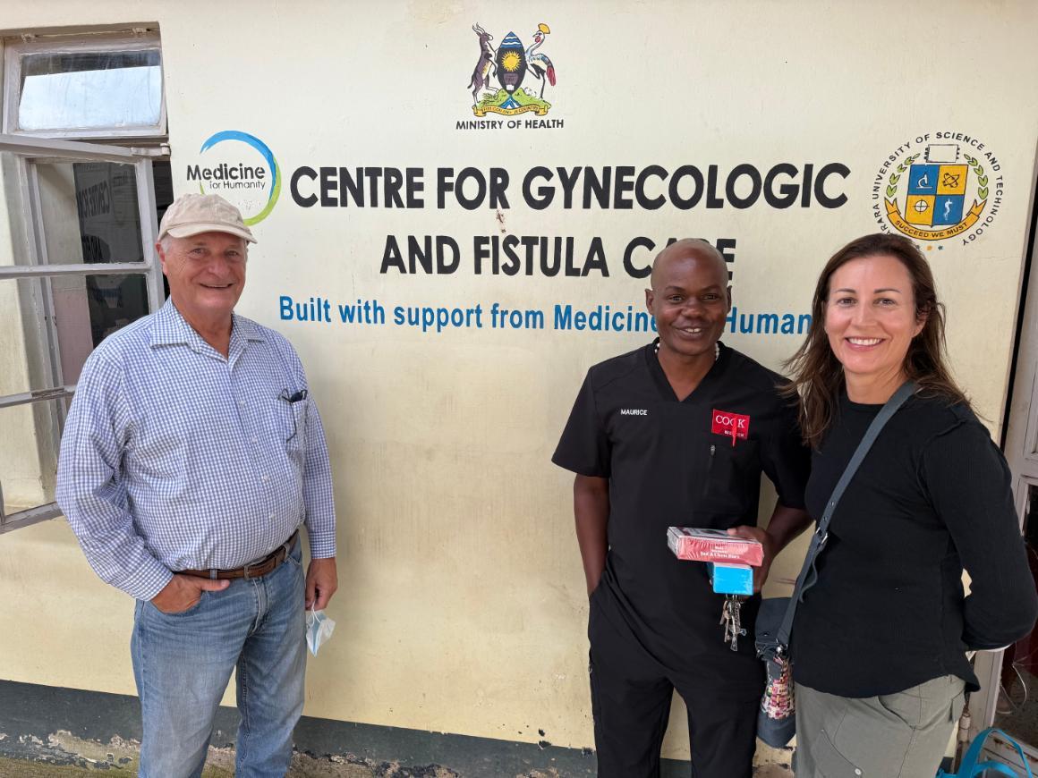 An older white man stands opposite a Black man and a white woman. All three are smiling. Text on the beige wall behind them reads Centre for Gynecologic and Fistula Care.