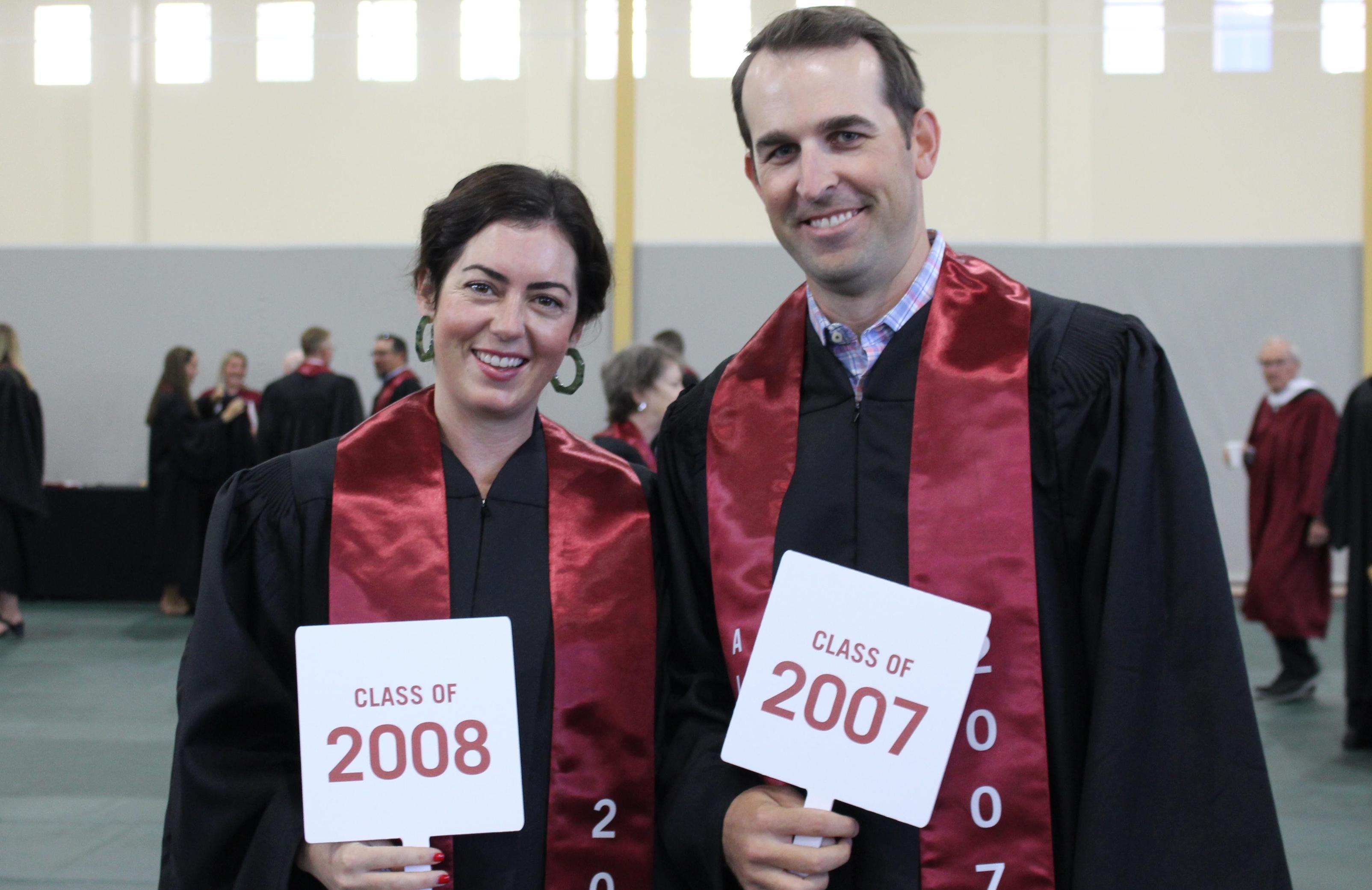 Two people in robes holding certificates at an event.