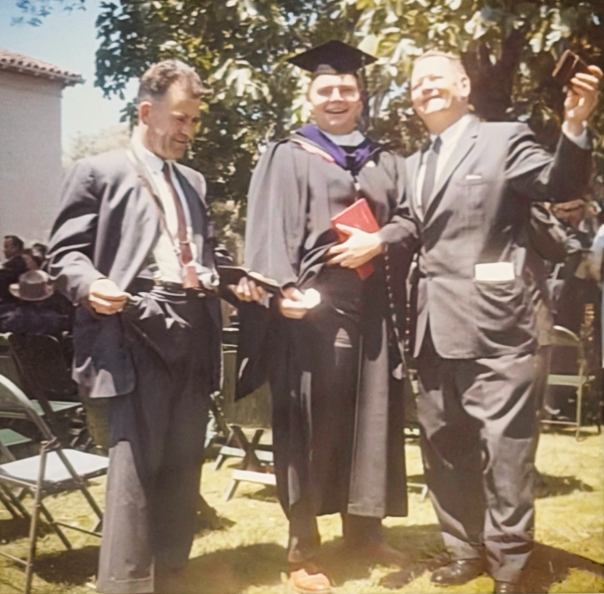 A 1963 photo of a young man in graduation regalia, standing with two men in suits and ties.