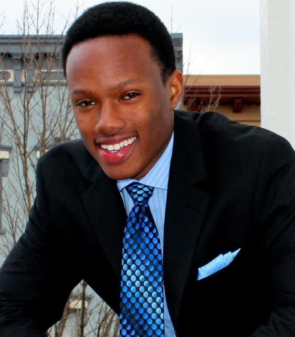 A person in a suit, smiling outdoors.