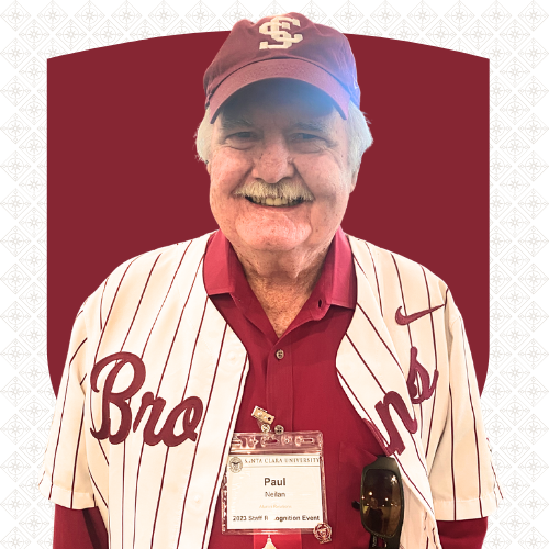 A smiling man in a Santa Clara University baseball cap and athletic shirt. His nametag reads Paul Neilan, Alumni Relations.